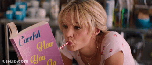 A Woman Drinking From A Straw While Reading A Book Titled Careful How You Go GIF