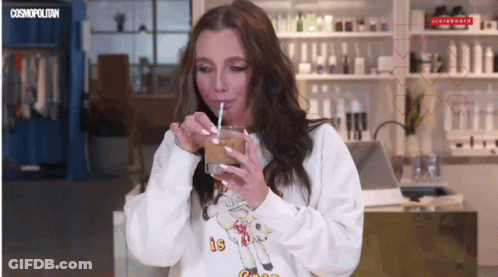 A Woman Drinking Through A Straw Wearing A Sweatshirt That Says Cosmopolitan On It GIF