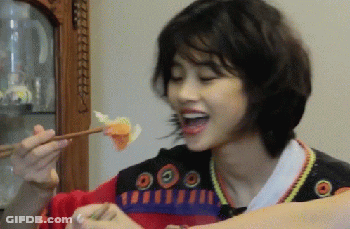 A Woman Eating A Piece Of Food With Chopsticks While Wearing A Sweater With Circles On The Front GIF