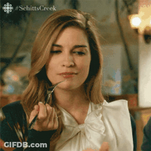 A Woman From Schitts Creek Is Eating With A Fork And Spoon GIF