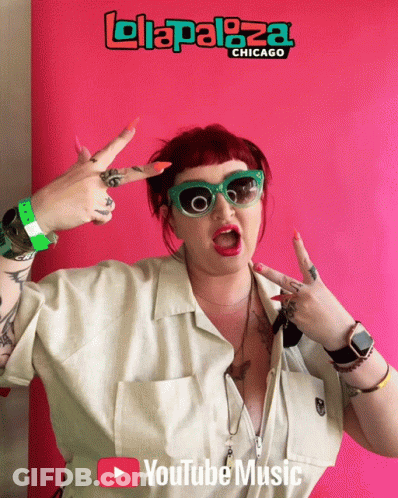 A Woman Giving A Peace Sign In Front Of A Sign That Says ' Lollapaloza Chicago ' GIF