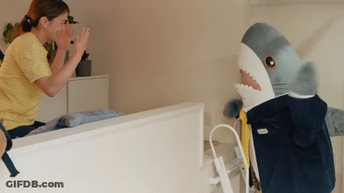 A Woman High Fives A Stuffed Shark That Is Wearing A Ikea Jacket GIF
