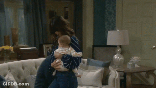 A Woman Holding A Baby In Her Arms In A Living Room GIF