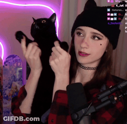 A Woman Holding A Black Cat In Front Of A Microphone With A Purple Background GIF