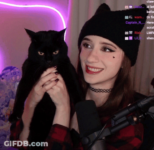 A Woman Holding A Black Cat In Front Of A Microphone With Captain_n Written On The Screen Behind Her GIF