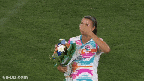 A Woman Holding A Bouquet Of Flowers And Wearing A Shirt That Says ' Uber Permanente ' On It GIF