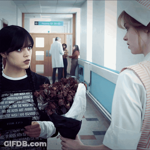 A Woman Holding A Bouquet Of Flowers In A Hallway With A Sign That Says Room Of 30-40 GIF