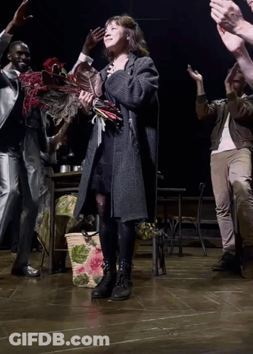 A Woman Holding A Bouquet Of Flowers Stands On A Stage GIF