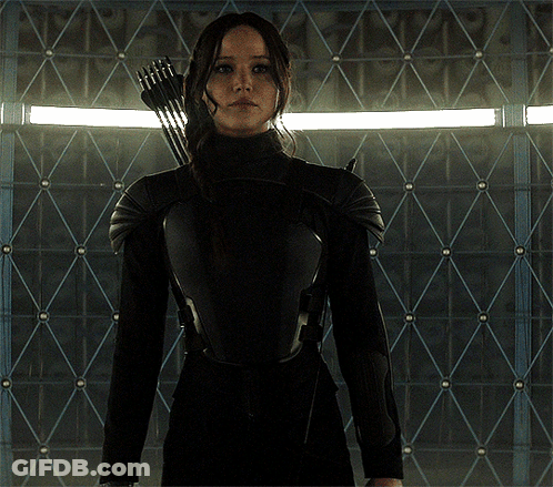 A Woman Holding A Bow And Arrow Stands In Front Of A Wall GIF