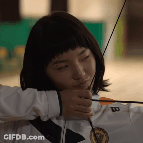 A Woman Holding A Bow And Arrow Wearing A White Wilson Jacket GIF