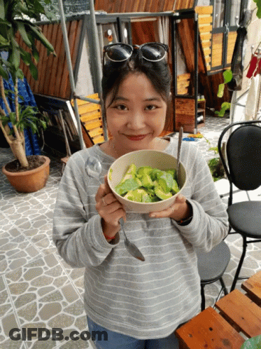 A Woman Holding A Bowl Of Food With A Spoon In Her Hand GIF