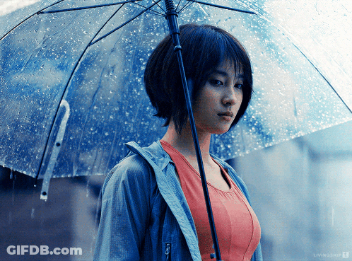 A Woman Holding A Clear Umbrella In The Rain With A Livingship Logo Behind Her GIF