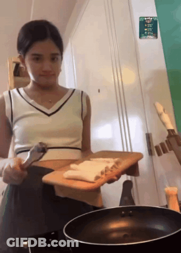 A Woman Holding A Cutting Board Next To A Frying Pan With A Sticker On The Wall That Says ' A ' GIF