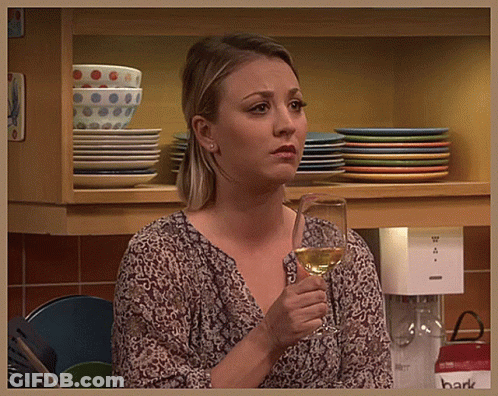 A Woman Holding A Glass Of Wine In Front Of A Shelf With Plates GIF