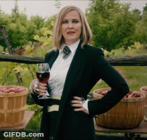 A Woman Holding A Glass Of Wine In Front Of Baskets Of Fruit GIF