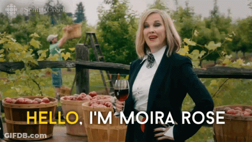 A Woman Holding A Glass Of Wine With The Words Hello I 'M Moira Rose GIF