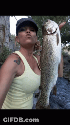 A Woman Holding A Large Fish With A Tattoo On Her Arm GIF