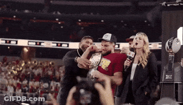 A Woman Holding A Microphone Stands Next To A Man In A Red Shirt That Says ' Nbc ' GIF