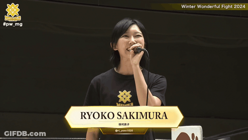 A Woman Holding A Microphone With The Name Ryoko Sakimura On The Screen GIF