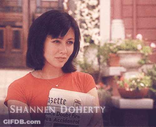 A Woman Holding A Newspaper With The Name Shannon Doherty Written On It GIF