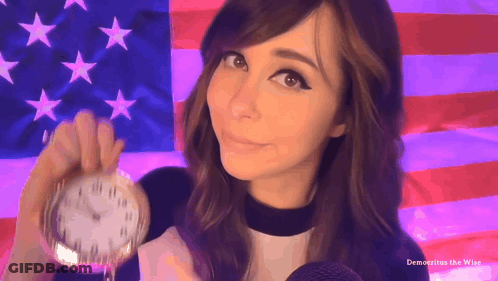 A Woman Holding A Pocket Watch In Front Of An American Flag With The Words Democritus The Wise Below Her GIF