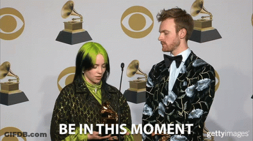 A Woman Holding A Trophy Next To A Man With The Words Be In This Moment On The Bottom GIF