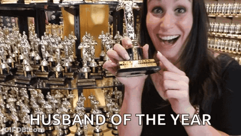 A Woman Holding A Trophy That Says " Husband Of The Year " GIF