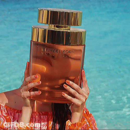 A Woman Holds A Bottle Of Michael Kors Perfume In Front Of Her Face GIF