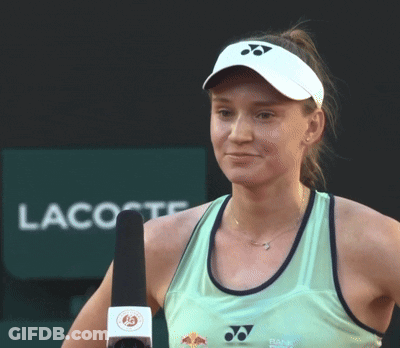 A Woman Holds A Microphone In Front Of A Lacoste Sign GIF