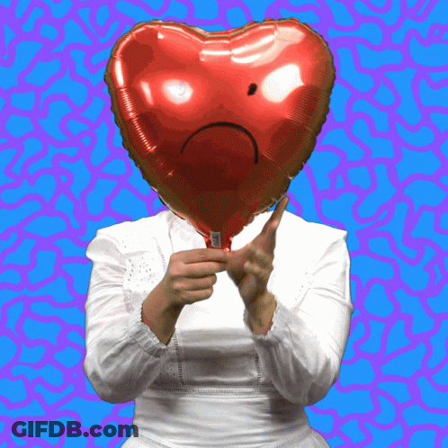 A Woman Holds A Red Heart Shaped Balloon With A Sad Face On It GIF