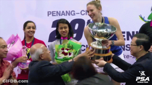 A Woman Holds A Trophy In Front Of A Penang-City Sign GIF