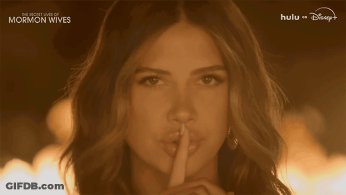 A Woman Holds Her Finger To Her Lips With The Words " The Secret Lives Of Mormon Wives " On The Bottom GIF