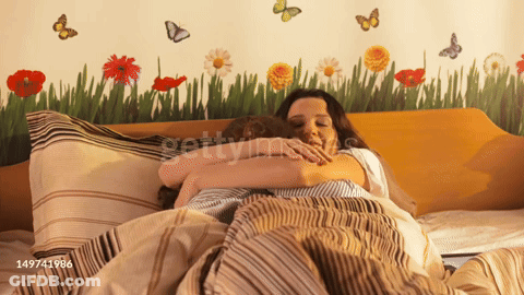 A Woman Hugging A Man In A Bed With A Wall With Flowers And Butterflies GIF