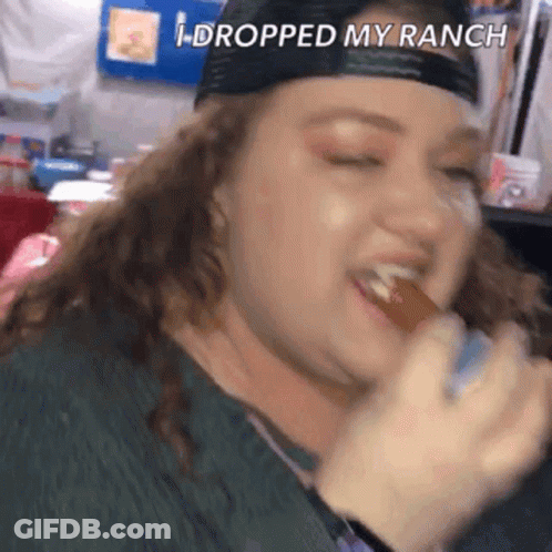 A Woman In A Baseball Cap Is Eating A Hot Dog With The Words I Dropped My Ranch Above Her . GIF