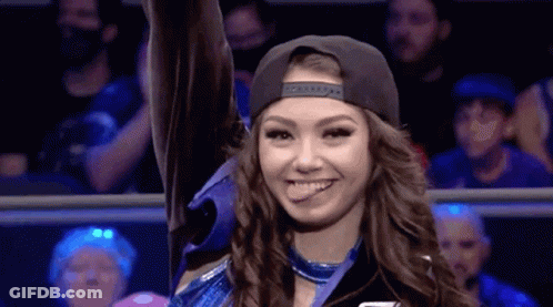 A Woman In A Baseball Cap Is Smiling And Holding Up Her Hand In A Ring . GIF