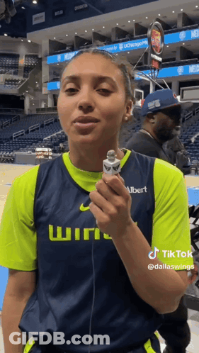 A Woman In A Basketball Uniform Is Holding A Microphone And Talking Into It . GIF