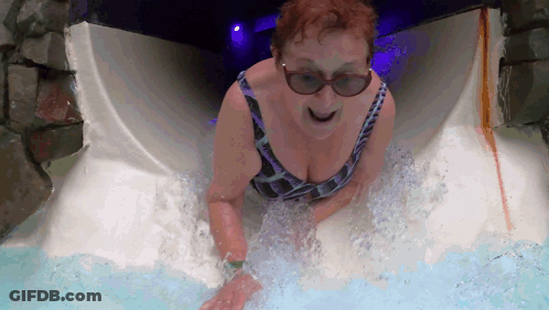 A Woman In A Bathing Suit And Sunglasses Slides Down A Water Slide GIF