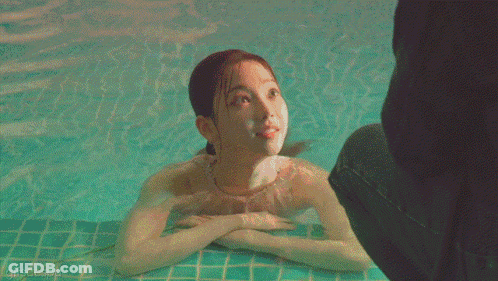 A Woman In A Bathing Suit Is Swimming In A Pool With A Person Standing Behind Her GIF