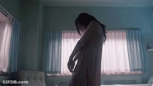 A Woman In A Bathrobe Is Standing In A Bedroom . GIF