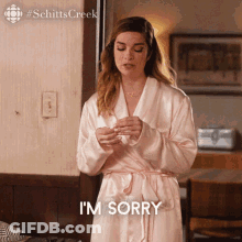 A Woman In A Bathrobe Is Standing In Front Of A Couch And Says I 'M Sorry . GIF