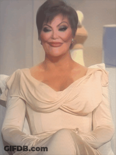 A Woman In A Beige Dress Is Sitting On A Couch With Her Arms Crossed GIF