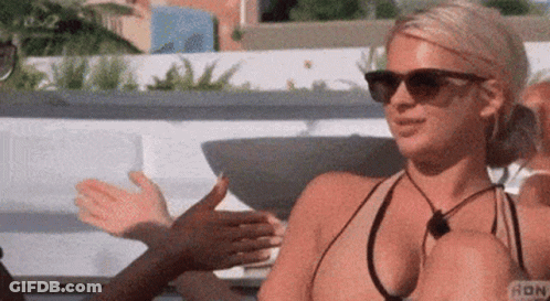 A Woman In A Bikini And Sunglasses Is Sitting On A Couch Talking To Another Woman . GIF