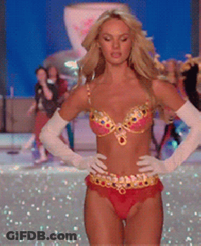 A Woman In A Bikini And White Gloves Is Walking On A Runway GIF