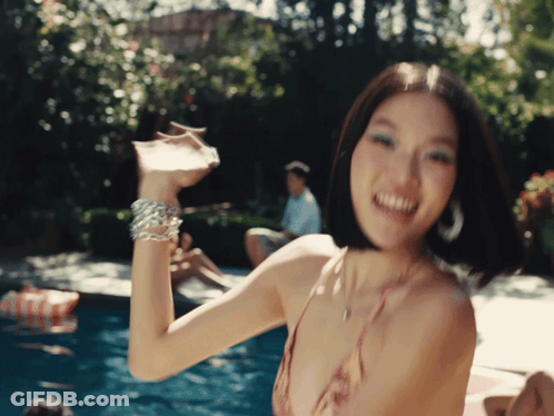 A Woman In A Bikini Holds A Drink In Her Hand In Front Of A Pool GIF