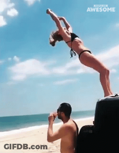 A Woman In A Bikini Is Doing A Handstand While A Man Drinks From A Cooler On The Beach GIF