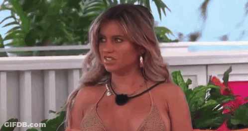 A Woman In A Bikini Is Sitting In Front Of A Fence And Plants . GIF