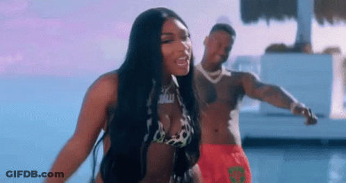 A Woman In A Bikini Is Standing Next To A Man In Red Shorts . GIF