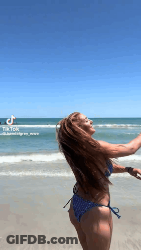 A Woman In A Bikini Is Standing On The Beach With Her Arms Outstretched . GIF