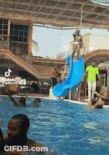 A Woman In A Bikini Is Standing On Top Of A Blue Water Slide In A Swimming Pool . GIF