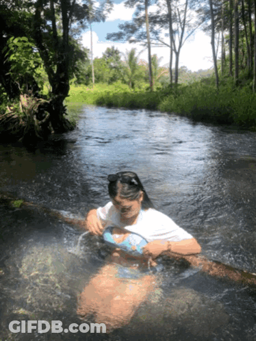 A Woman In A Bikini Is Swimming In A River With Trees In The Background GIF
